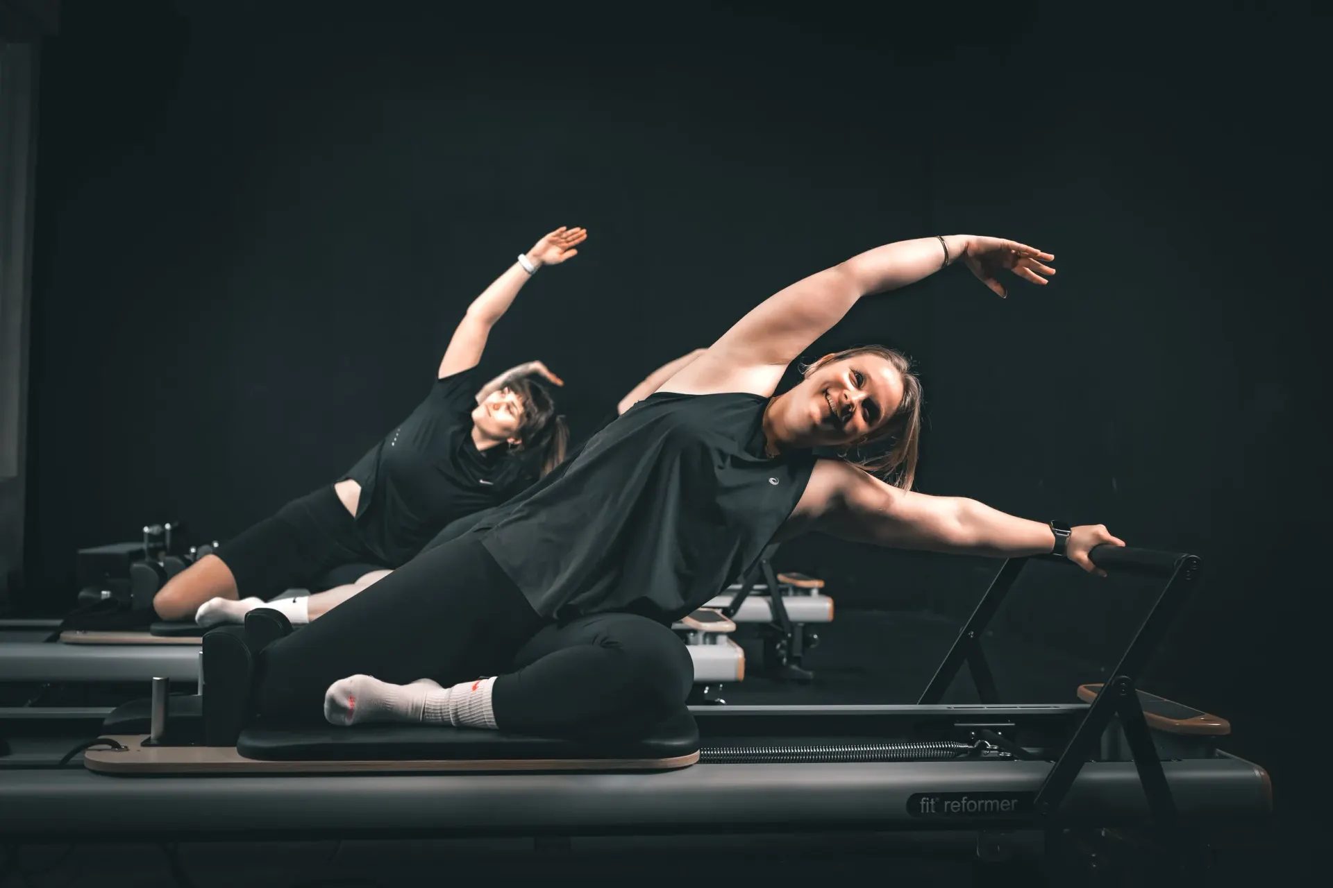 Twee vrouwen doen een zijwaartse stretch op de reformers tijdens een les bij Body Matrix in Rotterdam Katendrecht