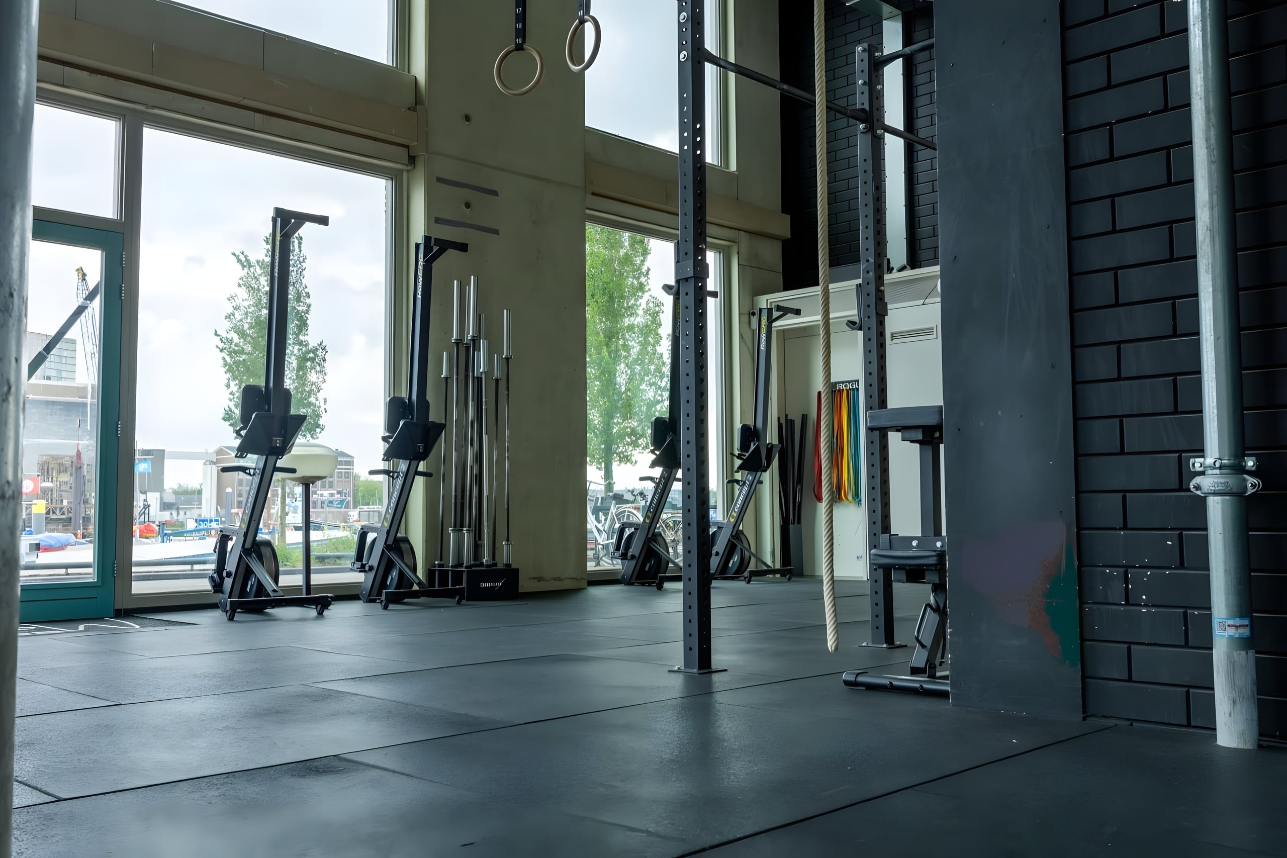 Conditioning hoek met turnringen, skiergs en hoge ramen met uitzicht op het water bij Body Matrix in Rotterdam Katendrecht